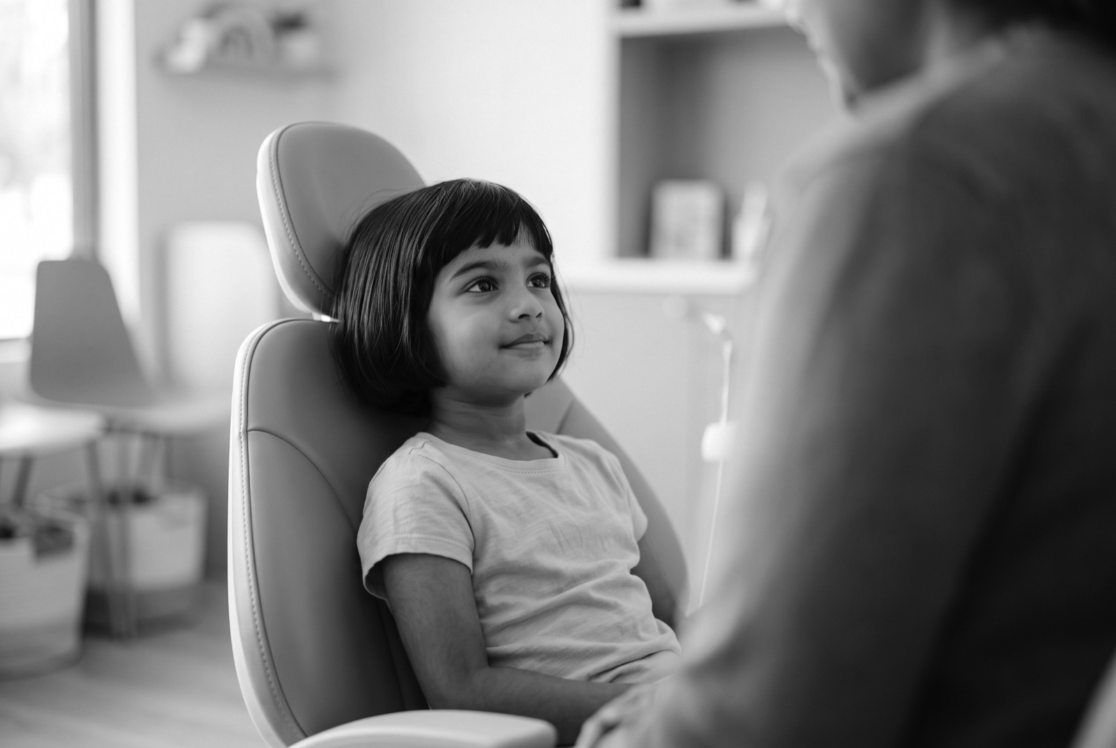 A young patient sitting calmly in the treatment chair with a parent beside her